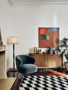 a living room with a black and white checkerboard rug, blue chair and large painting on the wall