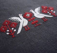 two white birds with red flowers on a gray background are embroidered onto the side of a piece of fabric