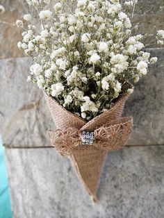 a bouquet of white flowers tied to a burlock hanging from a stone wall