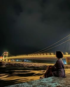 a person sitting on the edge of a rock looking at a bridge