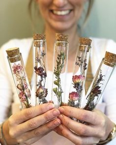 the woman is holding four glass vases with flowers in them