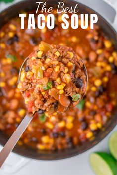 a spoon full of chili and corn soup with limes on the table behind it