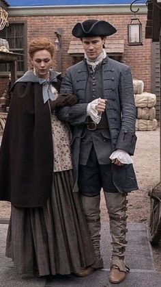 a man and woman dressed in period clothing standing next to each other on the street