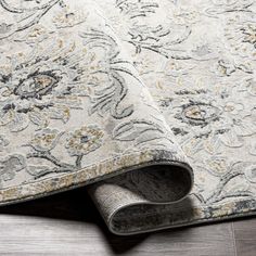 an area rug is laying on the floor next to a wooden floor with a gray and yellow floral design