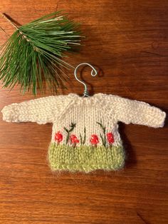 a knitted sweater ornament next to a pine branch on a wooden table