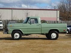 a green pick up truck parked in front of a large building with other trucks behind it