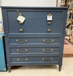 a blue chest of drawers with brass handles and knobs on display in a store