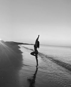 a woman doing yoga on the beach in front of the ocean with her arms up