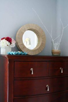 a dresser with flowers, vases and a round mirror on it's top