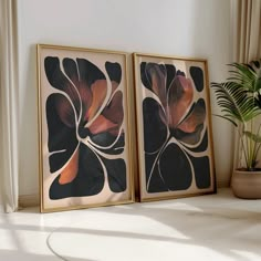 two framed art pieces sitting on top of a table next to a potted plant