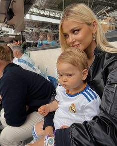 a woman sitting next to a little boy at a soccer game with fans in the stands