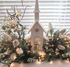 a small church surrounded by christmas decorations and lights in front of a window with shutters