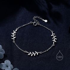 a silver bracelet with leaves and water drop on it, sitting next to blue flowers