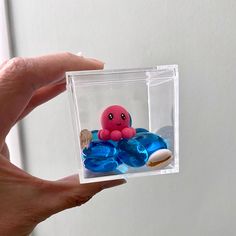 a hand holding a small plastic toy with an octopus on it's back in a clear box