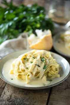 a plate of pasta with sauce and parsley on the side next to some bread