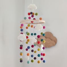 a multicolored cloud mobile hanging from a white wall next to a wooden clock