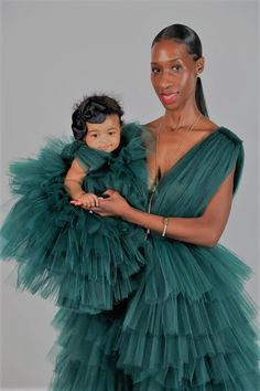 a woman in a green dress holding a baby wearing a ruffled gown and necklace