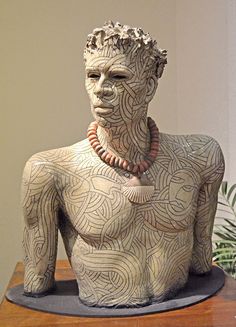 a sculpture of a man with beads on his neck and chest sitting on a table