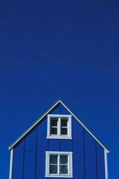 the top of a blue house with white trim and windows against a bright blue sky