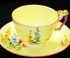 a yellow tea cup and saucer with flowers on the rim, sitting on a black background