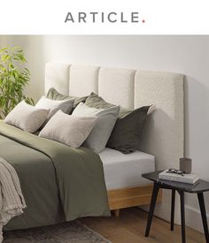 a bed with green sheets and pillows in a bedroom next to a plant on a table