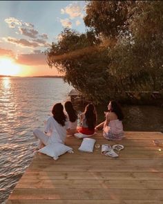 three women sitting on a dock watching the sunset