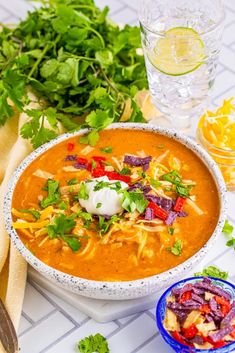 a white bowl filled with soup next to two bowls of chips and cilantro