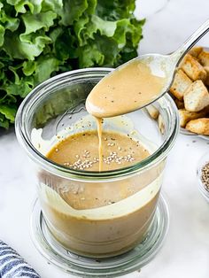 a spoon pouring dressing into a glass bowl filled with breadcrumbs and vegetables