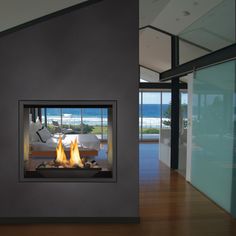 a fire place in the middle of a room with glass walls and doors leading to an ocean view