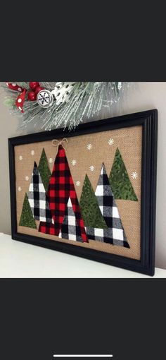 a christmas tree is hanging on the wall in front of a framed canvas with plaid trees and snowflakes