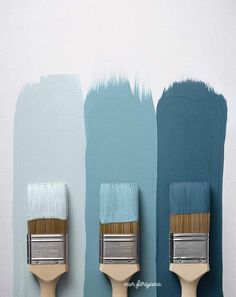 three paintbrushes with different shades of blue and green painted on the wall behind them