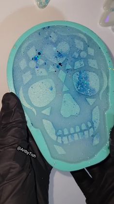 a person in black gloves holding a skull shaped ice tray with blue bubbles on it