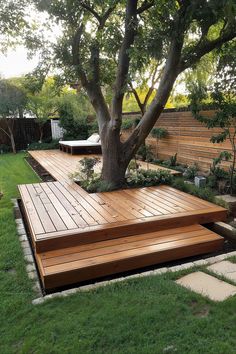 a large wooden deck in the middle of a grassy area next to a tree and fence