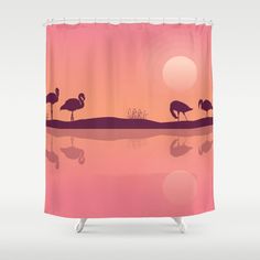 two flamingos are standing in the water at sunset