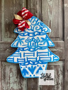 a blue and white ceramic christmas tree ornament hanging on a wooden door with a red bow