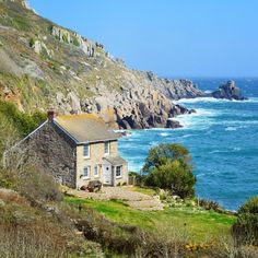 an old house sitting on the side of a cliff next to the ocean with blue water