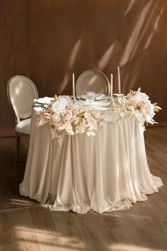 a table with flowers and candles on it in front of a brown wall, surrounded by chairs