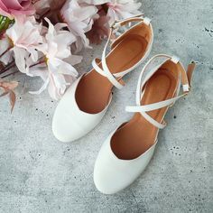 a pair of white shoes sitting on top of a cement floor next to pink flowers