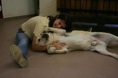 a woman is laying on the floor with her dog, who is cuddling her