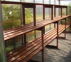 a long wooden bench sitting inside of a glass walled room next to a brick floor