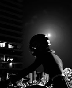 black and white photograph of a person riding a bike at night in front of a building