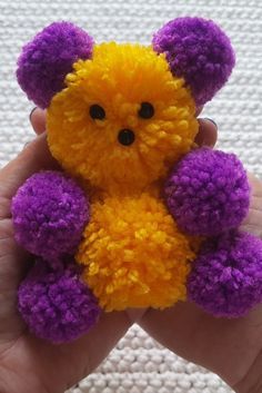 a hand holding a yellow and purple teddy bear