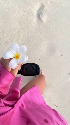 a person holding a flower in their hand while laying on the sand at the beach