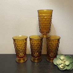 four yellow glass vases sitting on top of a table next to a succulent plant