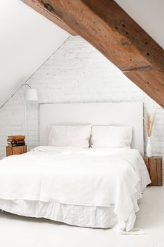 a white bed sitting under a wooden beam in a bedroom