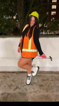 a woman wearing an orange safety vest and white socks is dancing in front of a wall