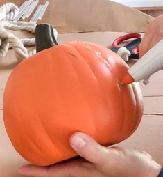 a person is using scissors to cut the top of an orange pumpkin with pliers