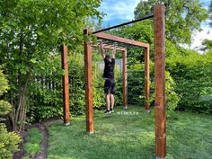 a man is standing in the middle of a yard with his arms up on a wooden structure