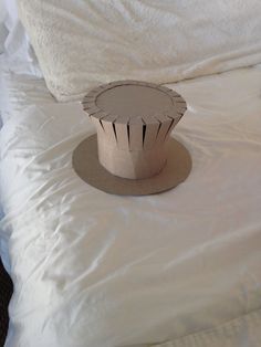 a hat sitting on top of a bed with white sheets and pillows in the background