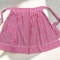 a red and white gingham apron on a wooden floor with a tie around the waist